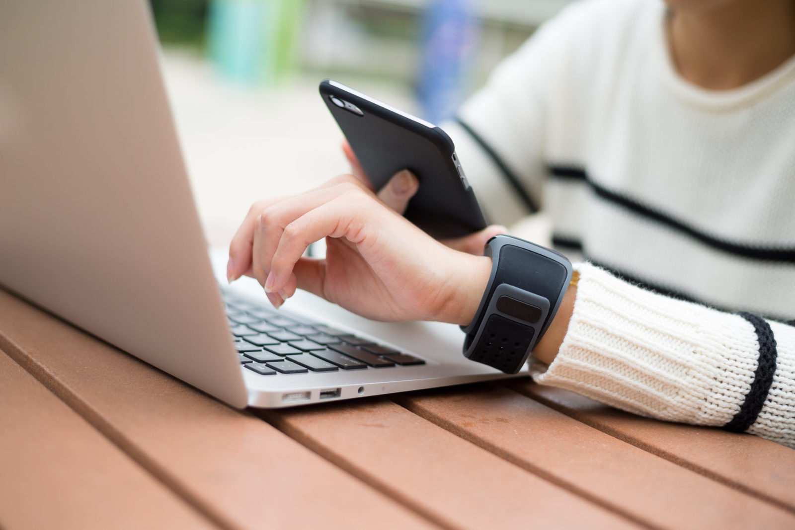 A close-up of a person's left hand hovering over a laptop keyboard. The other hand holds a smart phone.